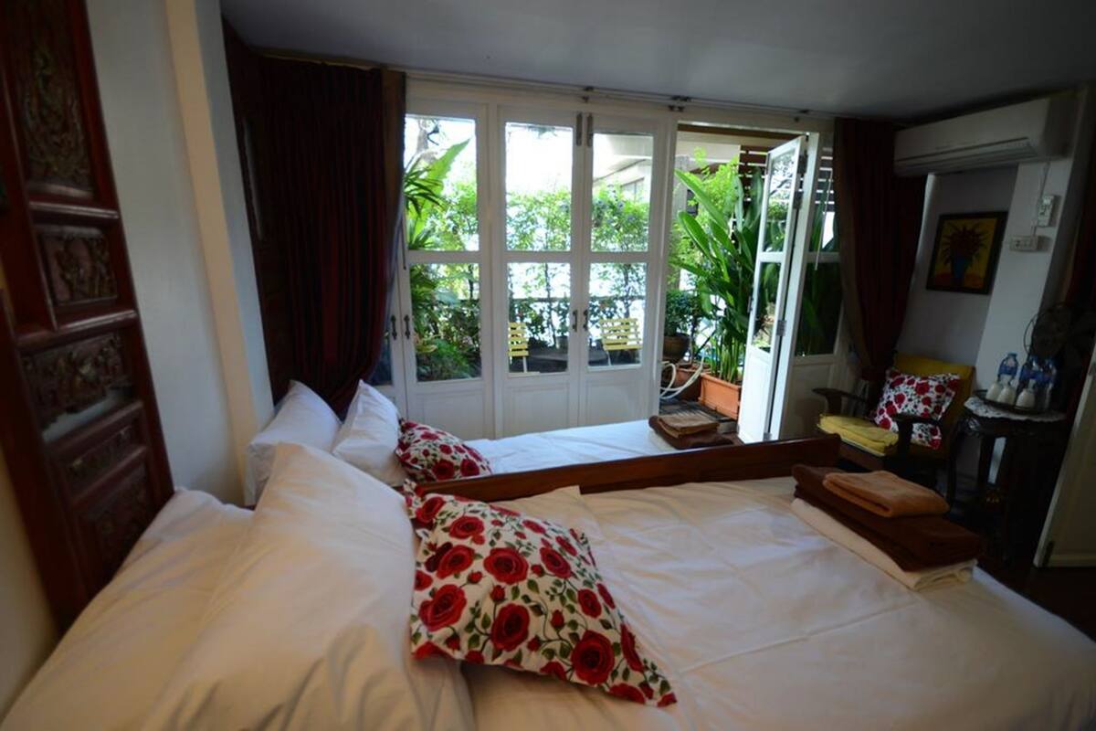 A hotel room with two beds, a large window with a view of the garden, and a small table with a chair.