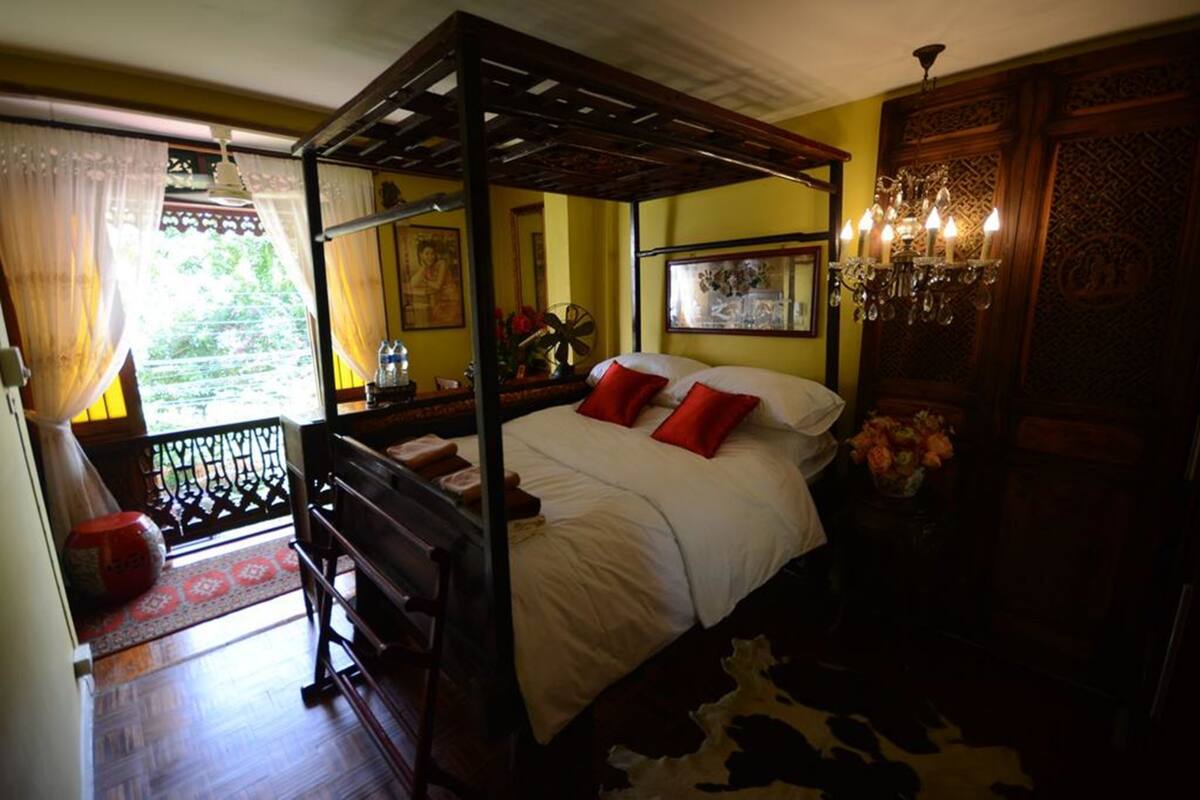 A four-poster bed with red pillows, a chandelier, and a cowhide rug.