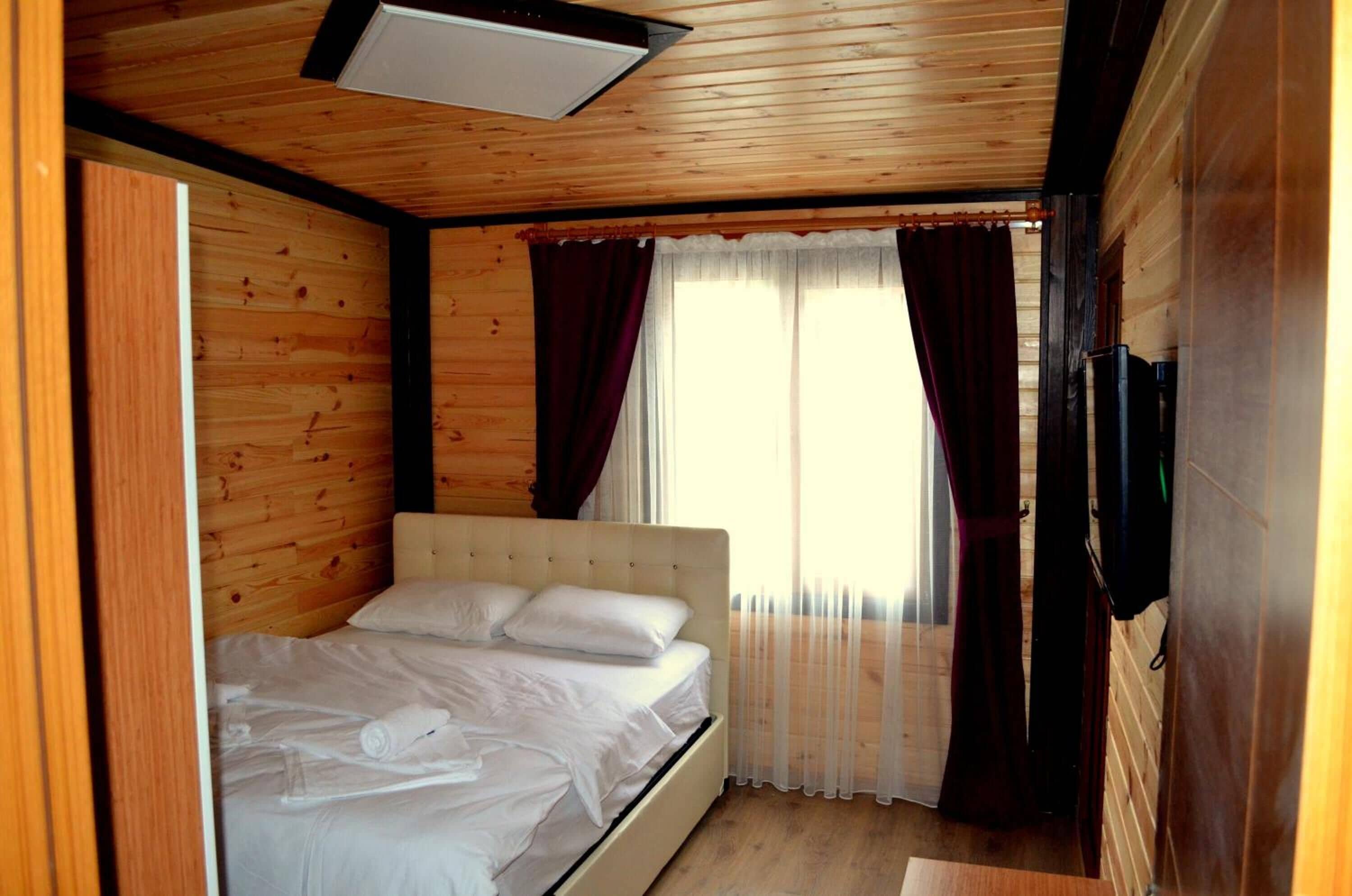 A wooden-paneled room with a bed, curtains, and a ceiling light.