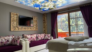 A room with a ceiling mural, a TV mounted on a wooden frame, a sofa with floral cushions, a bed, and a window with curtains. - Osmanli Suite (Çaykara)