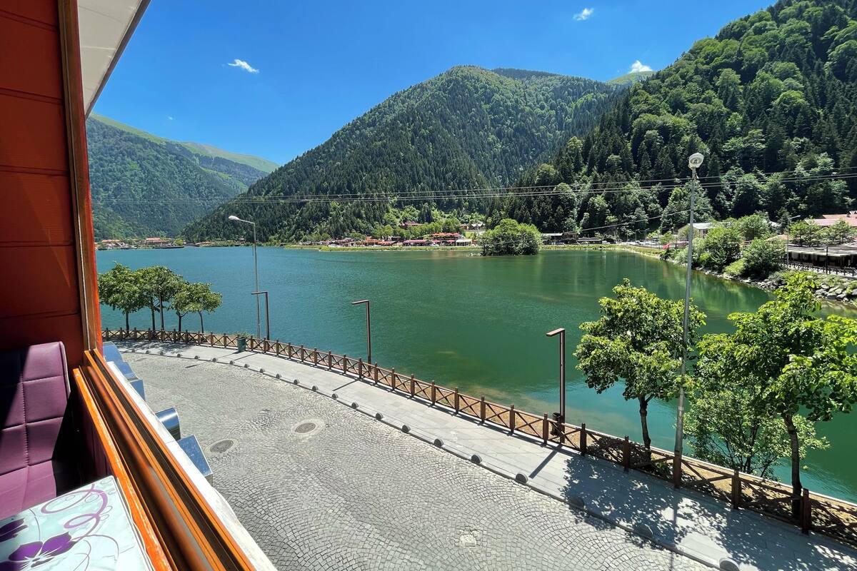 A view of a lake with mountains, a wooden fence, and a paved walkway.