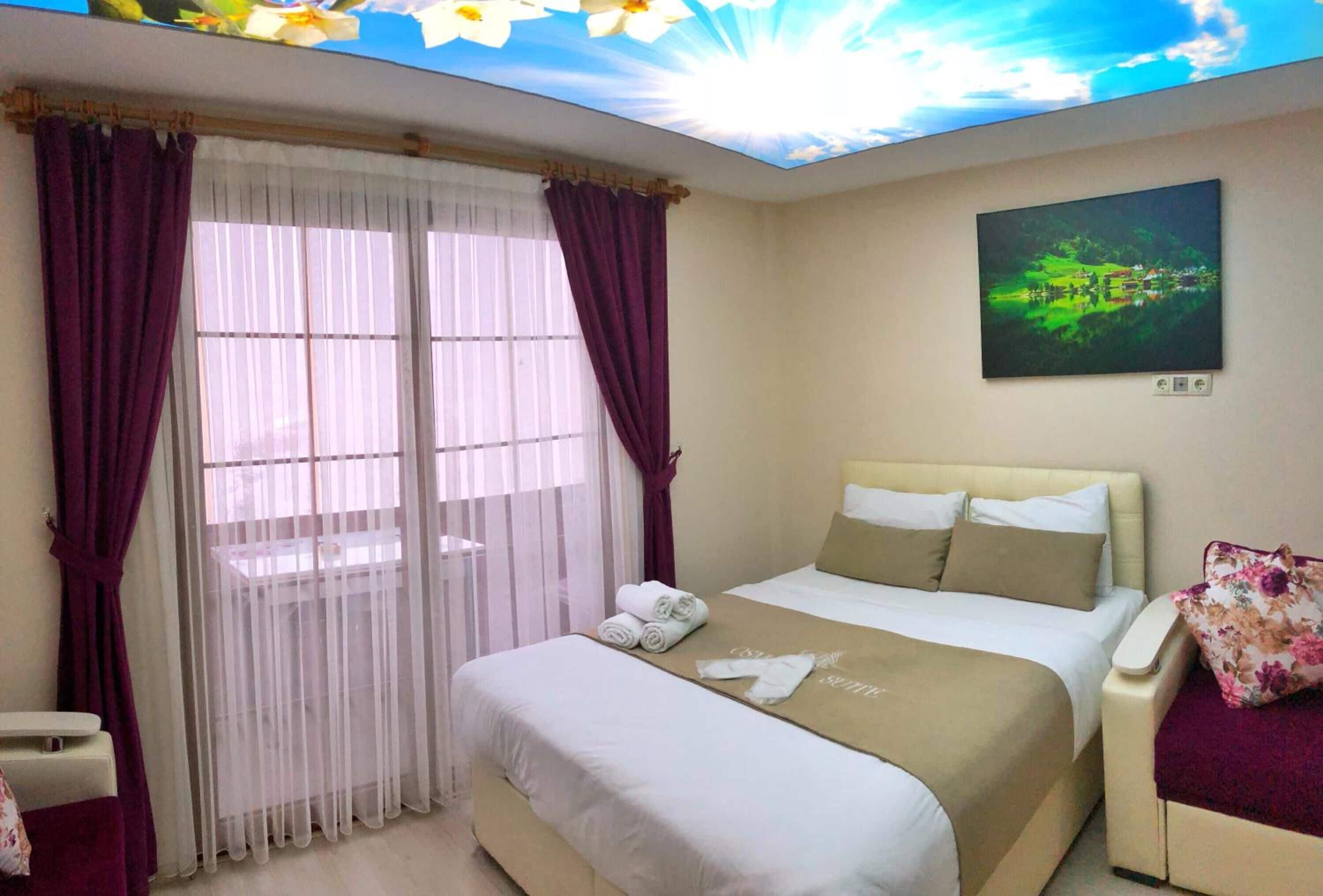 Una habitación de hotel con una cama, una silla, una ventana con cortinas y un cuadro en la pared.