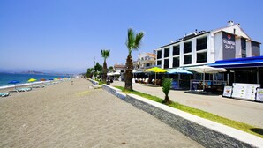 Un hotel frente a la playa con asientos al aire libre y sombrillas, vista despejada al mar, y un letrero que dice 'Olympia Beach Club'.