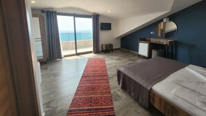 Un dormitorio con una cama grande, un escritorio de madera, un espejo y vistas al mar a través de una puerta corredera.