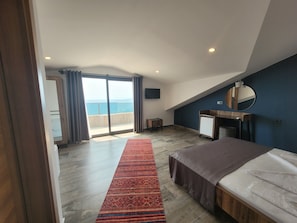 A bedroom with a large bed, a wooden desk, a mirror, and a view of the sea through a sliding door. - Olimpia Hotel (Fethiye)