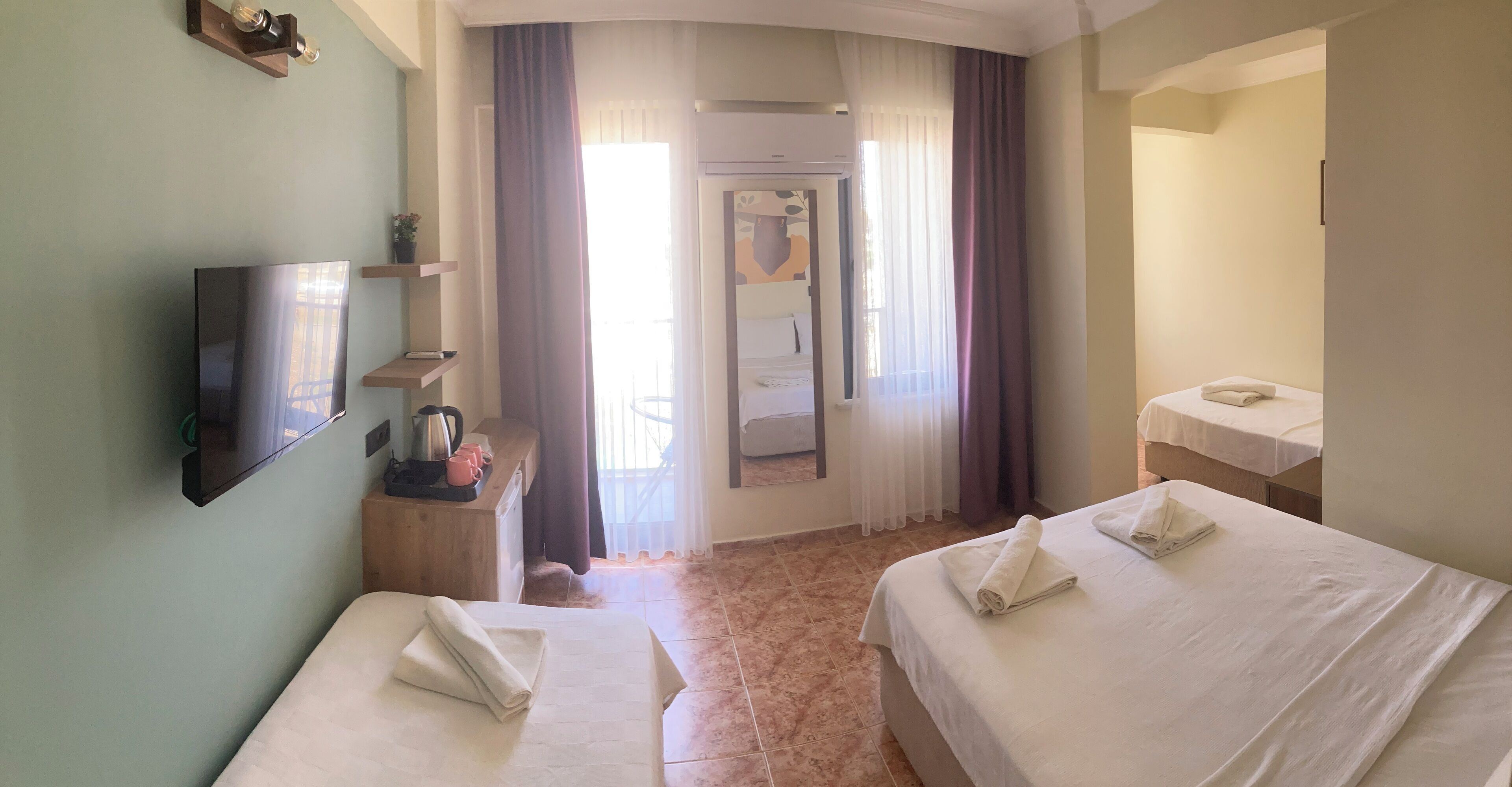 A hotel room with two beds, a TV, a desk with a kettle, and a bathroom with a mirror and towel.