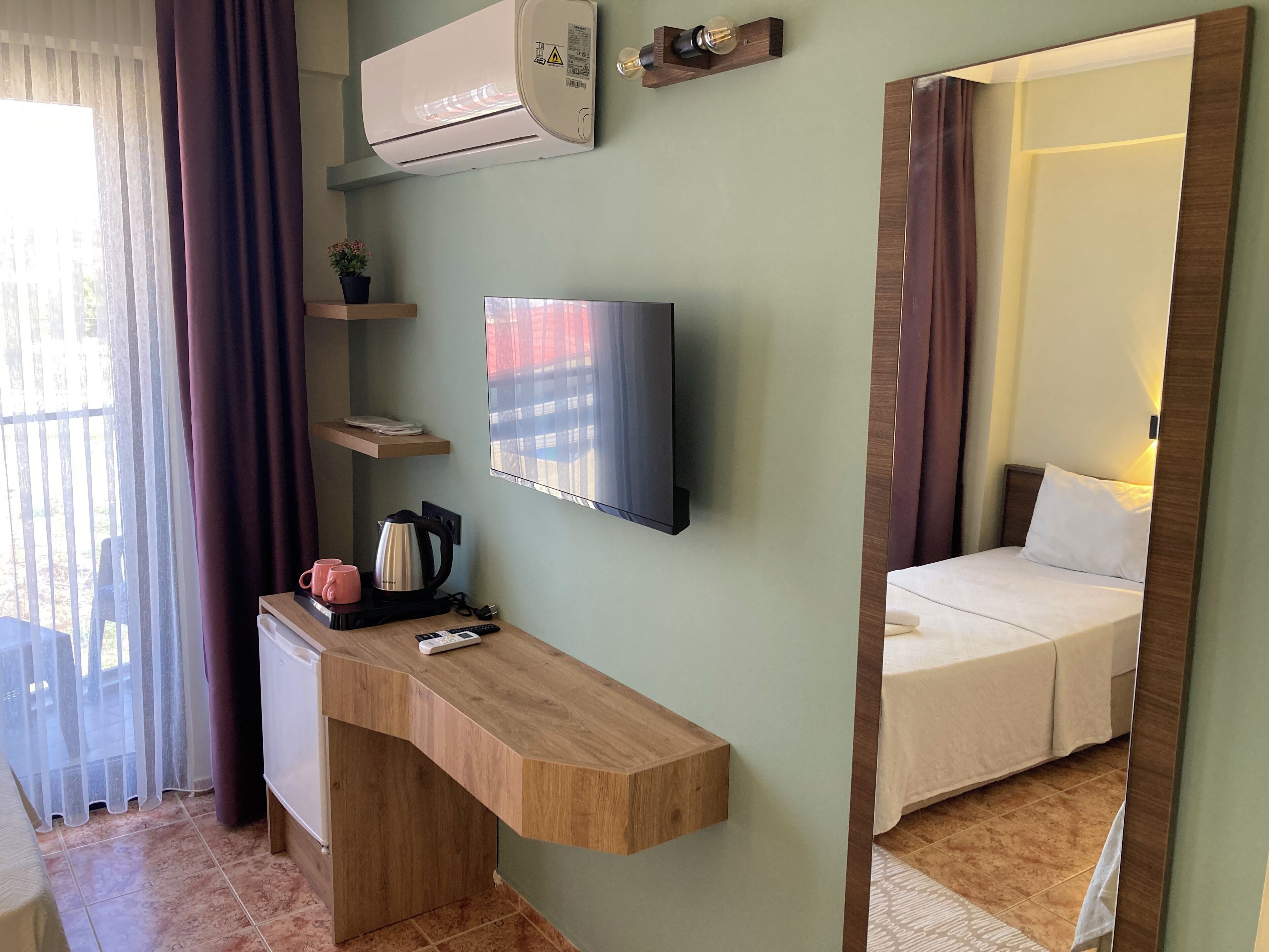 Une chambre d’hôtel avec un bureau en bois, un téléviseur à écran plat, un lit, un climatiseur et une fenêtre avec des rideaux.