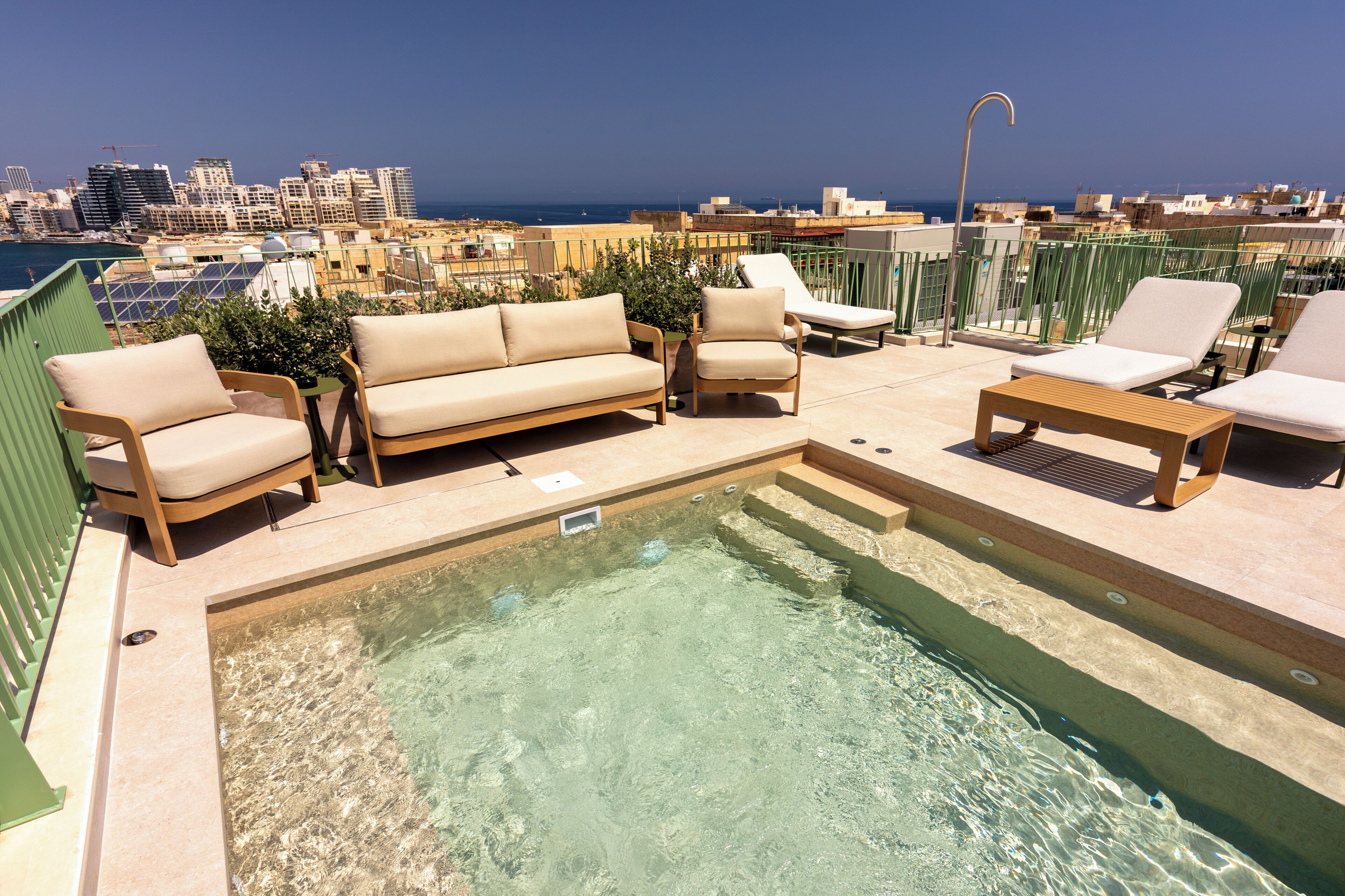 Área de piscina en la azotea con sillones de descanso, un sofá y vistas panorámicas de la ciudad.
