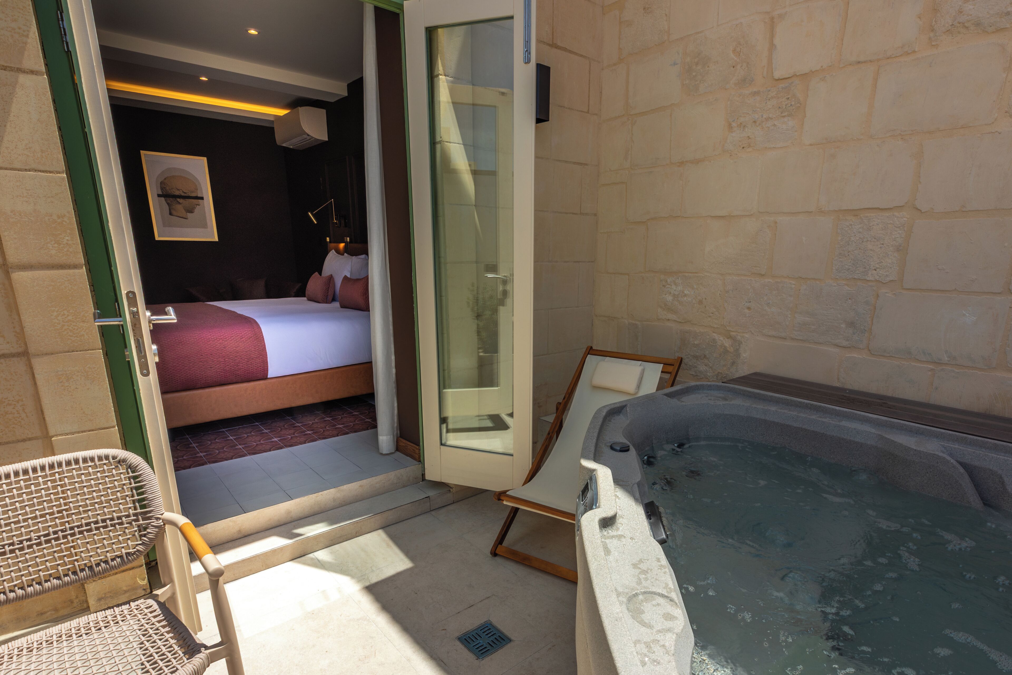 A room with a bed, a glass shower enclosure, a bathtub, and a wicker chair.