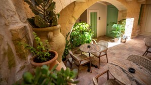 A courtyard with stone walls, potted plants, wicker furniture, and a door with a green frame. - The Vincent Boutique Hotel, BW Premier Collection (Valletta)
