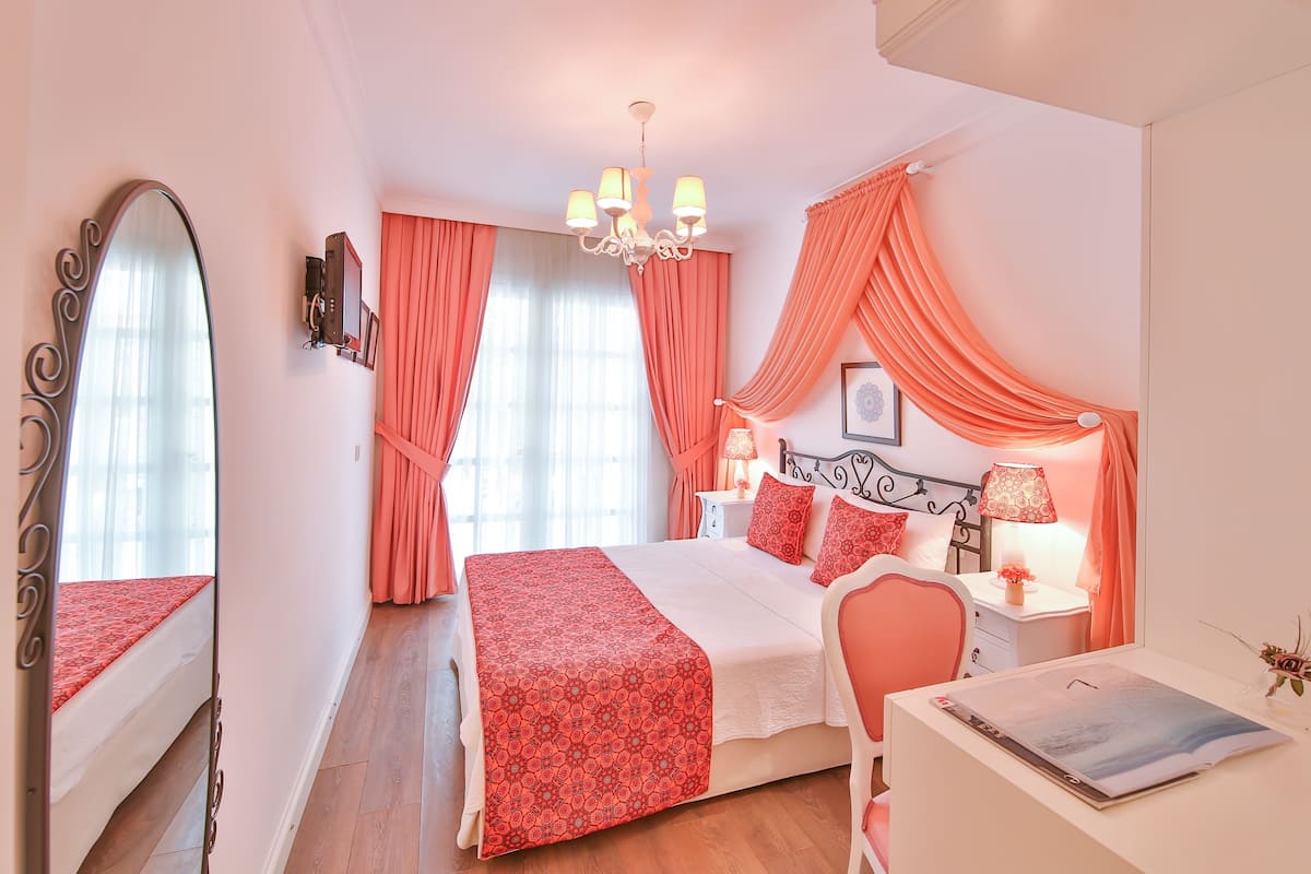 A bedroom with a bed, a desk, a chair, a mirror, a chandelier, and curtains.