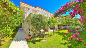 A stone building with a white balcony, surrounded by lush greenery and flowering plants. - Alacati Sorf Hotel (Cesme)