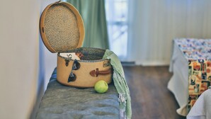 A suitcase with a patterned interior, a green apple, and a blanket on a bench in a room with a bed in the background. - Alacati Sorf Hotel (Cesme)