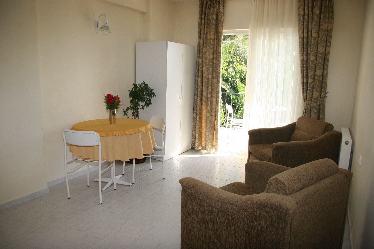 A living room with a dining area, a white refrigerator, and a plant.