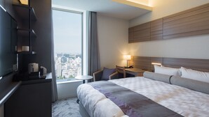 Habitación de hotel moderna con una cama grande, un escritorio, una silla, un televisor y vistas a la ciudad.