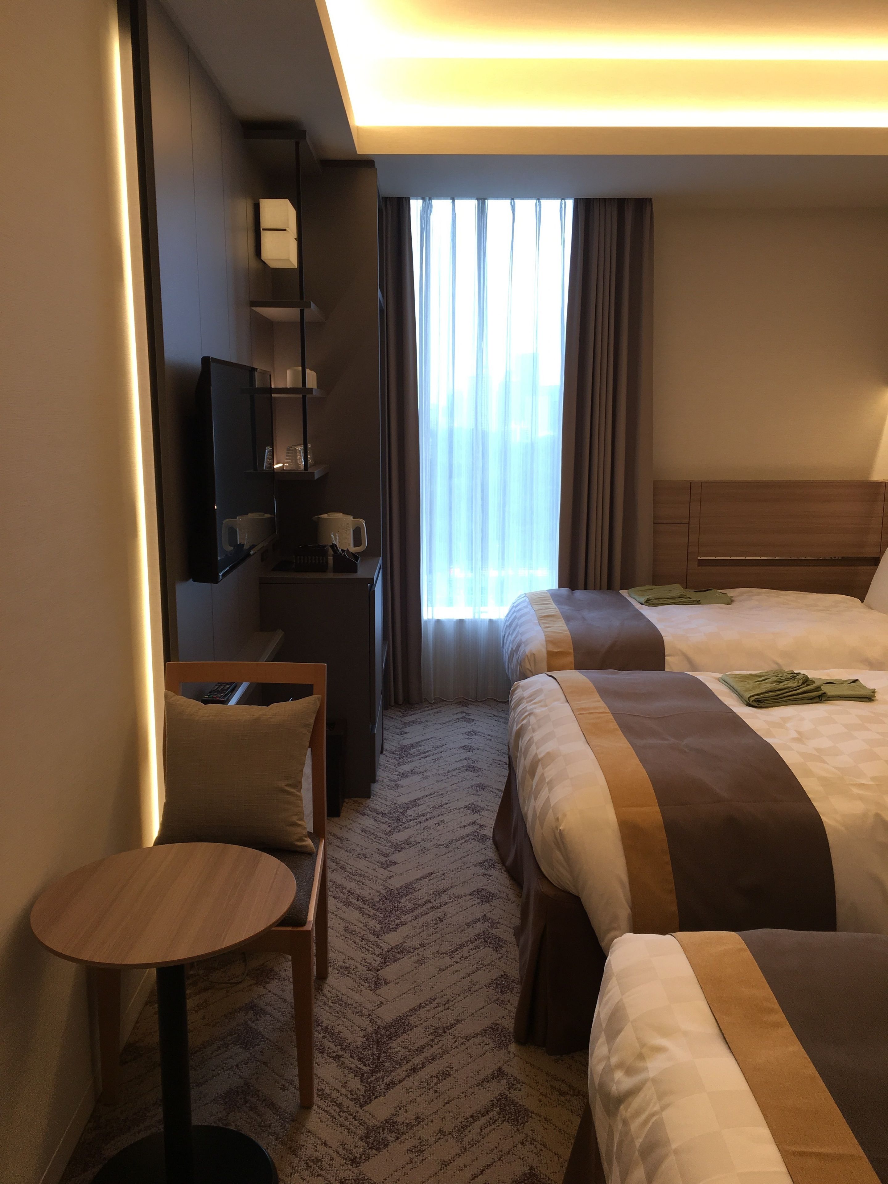 A hotel room with two beds, a small table, a TV, and a window with curtains.