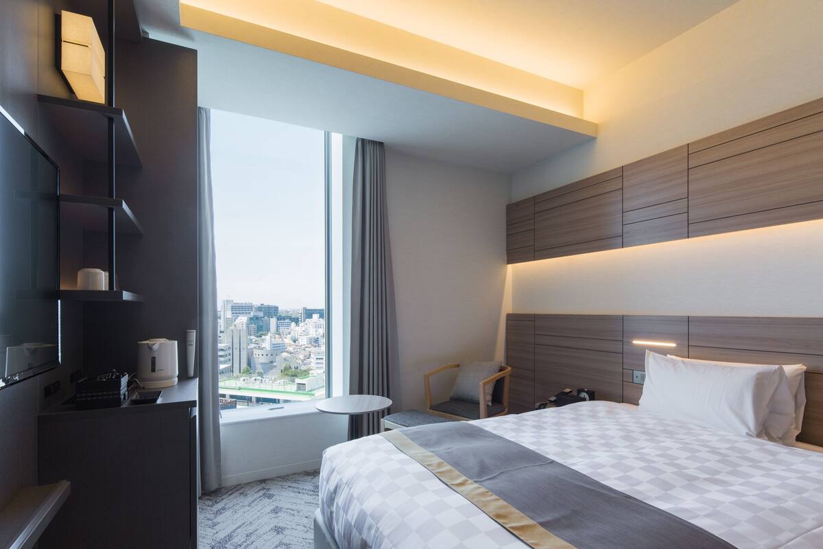 A modern hotel room with a large bed, a desk, and a view of the city.
