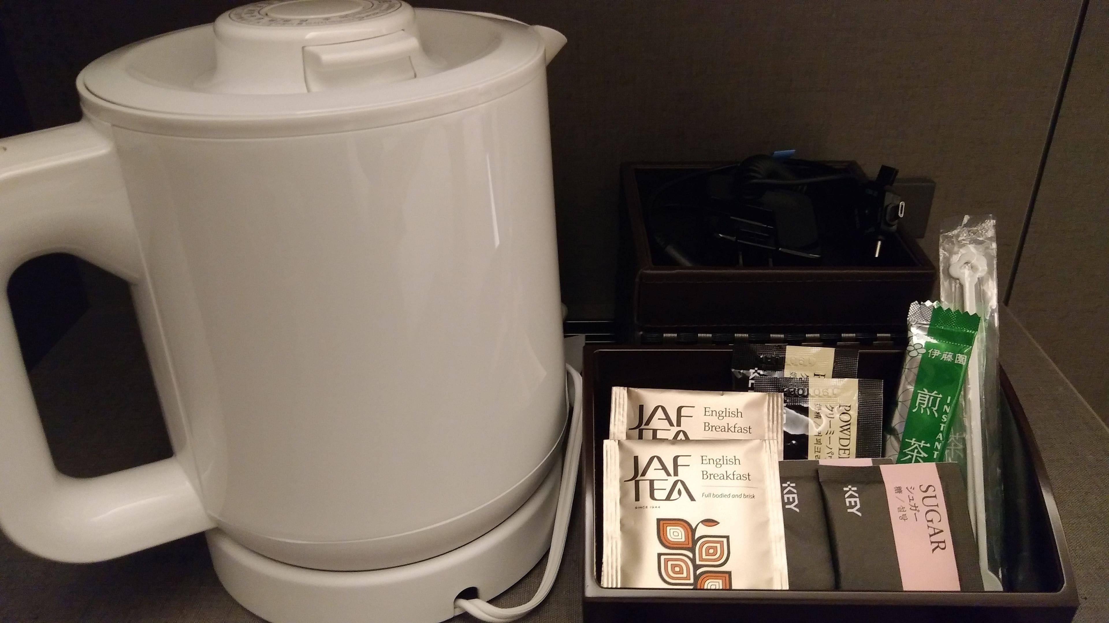 En kaffebryggare, ett fat med tepåsar och en förpackning socker i ett hotellrum.