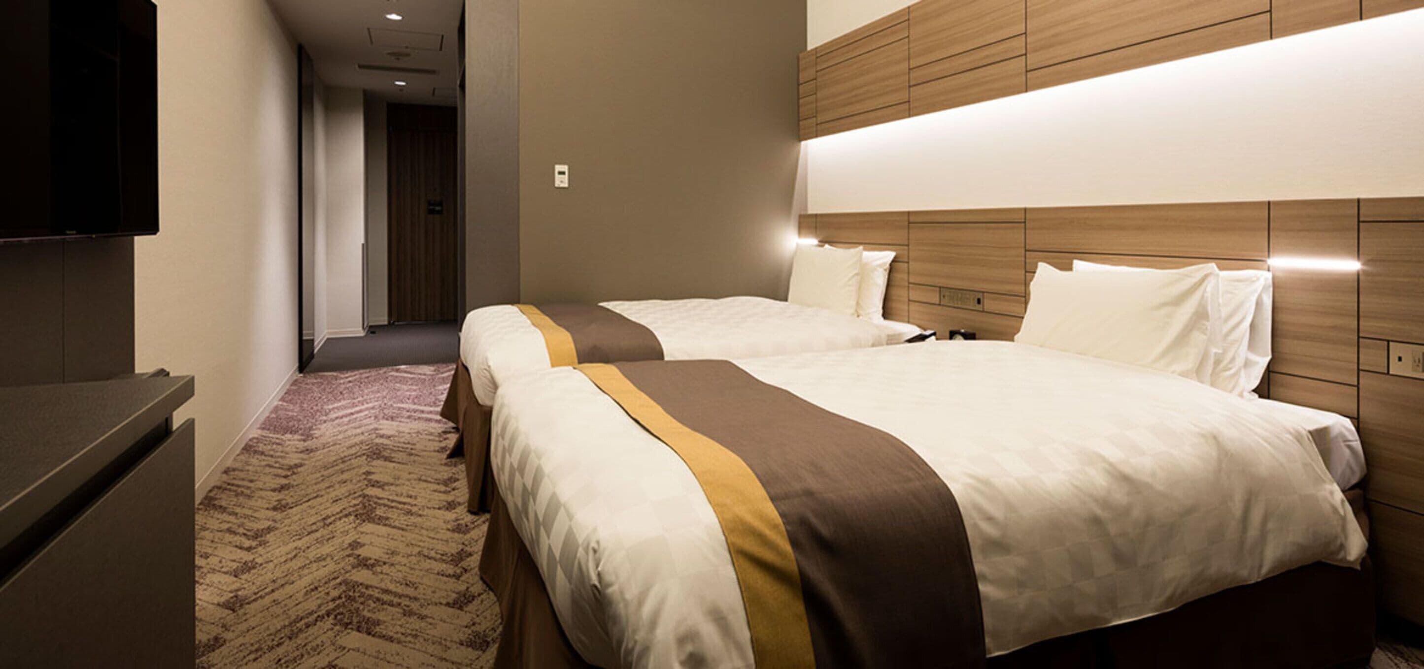 Habitación de hotel con dos camas, un televisor de pantalla plana y piso alfombrado.