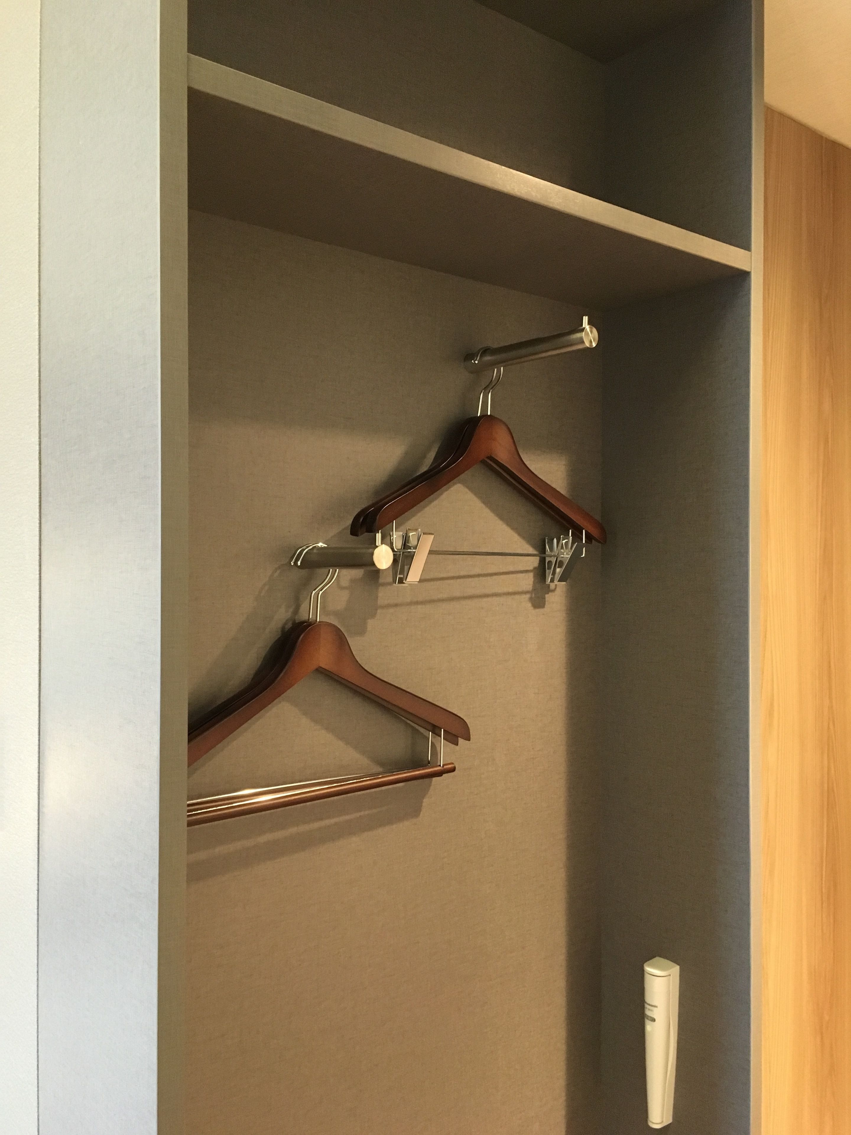 A closet with wooden hangers and a white appliance, likely a refrigerator, against a grey wall.
