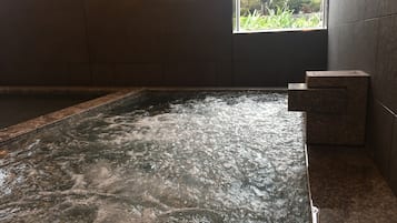 Banheira de hidromassagem com água corrente, rodeada por paredes azulejadas e uma janela com vista para vegetação.