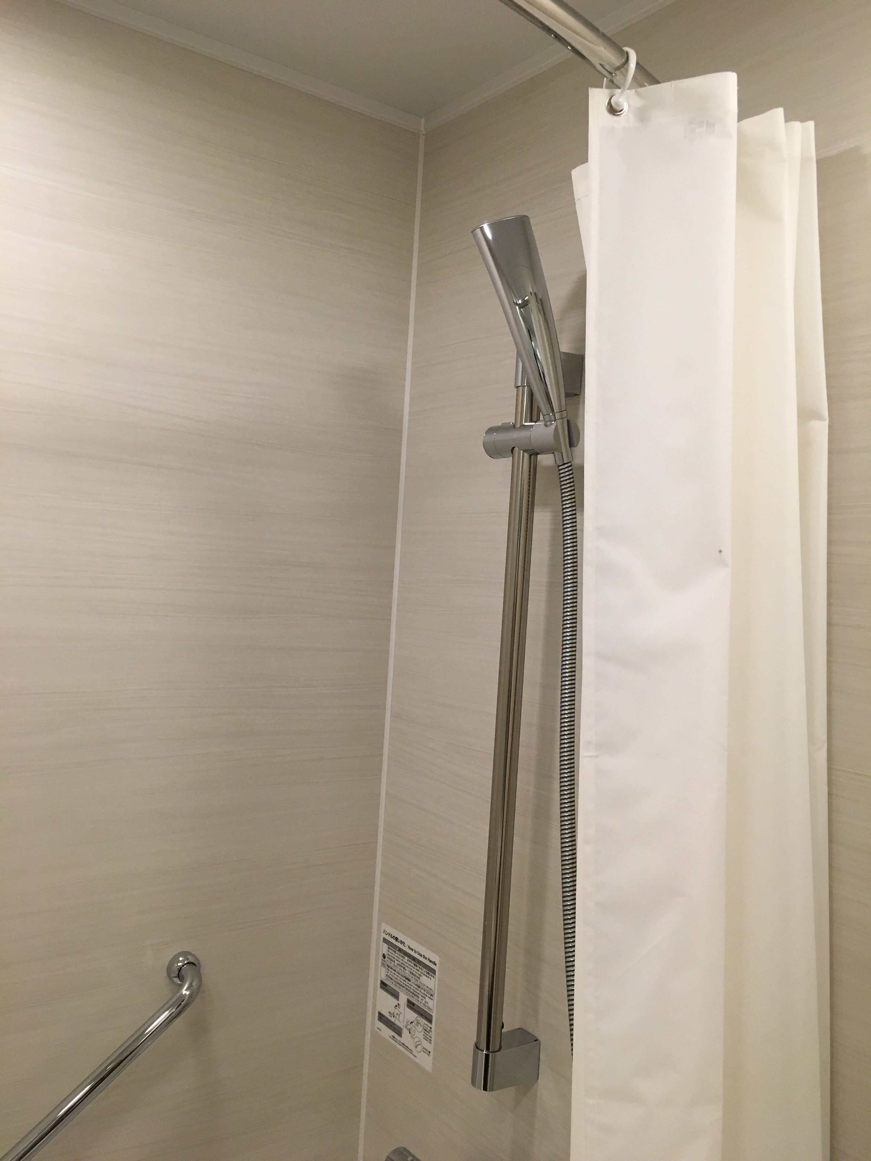 A shower area with a handheld showerhead, a vertical rain showerhead, and a shower curtain.