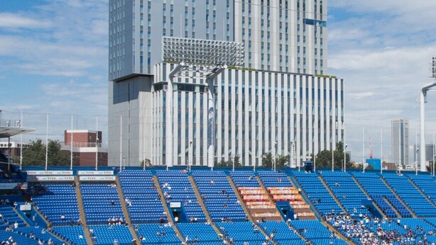 Un estadio con asientos azules y un edificio moderno al fondo.
