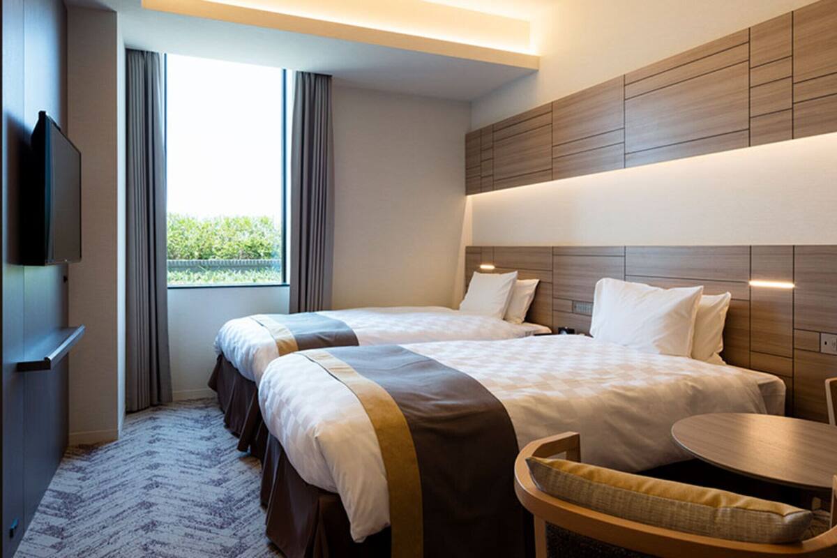 A hotel room with two beds, a television, a small table, and a chair.