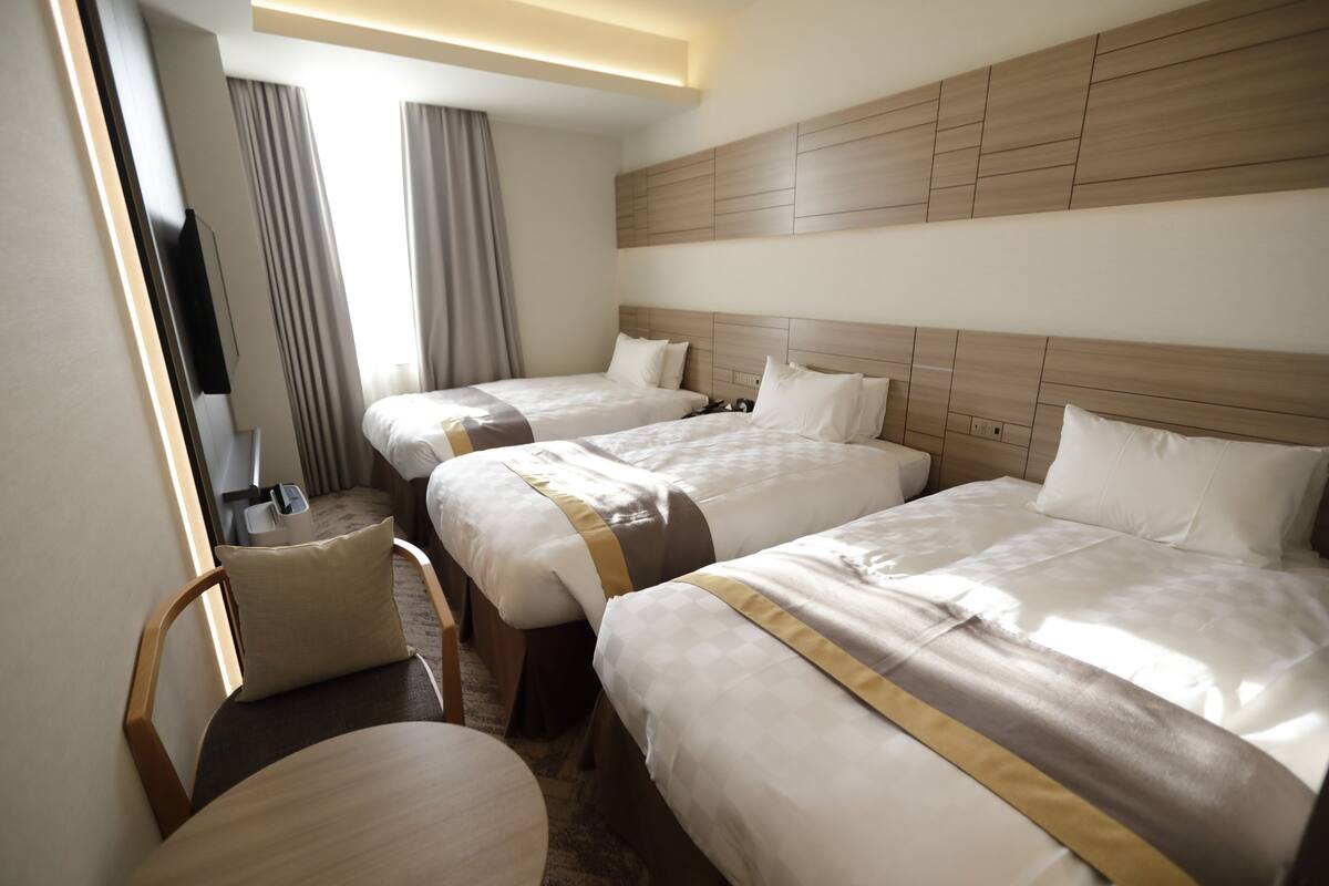 A hotel room with three beds, a TV, and a small table.