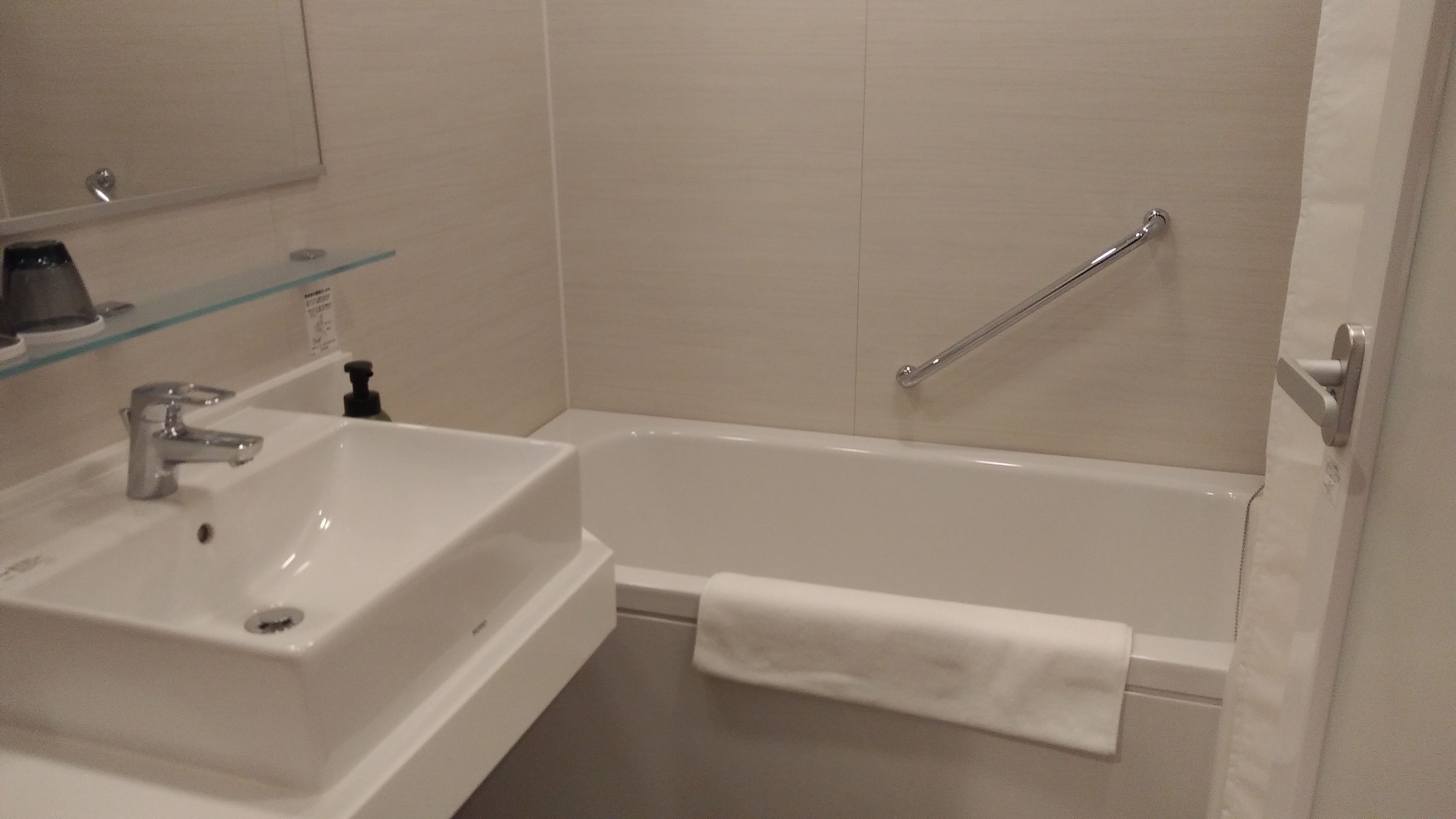 A bathroom with a white sink, a mirror, and a glass shelf.