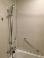 A bathroom with a bathtub, a shower with a handheld showerhead, and a grab bar.