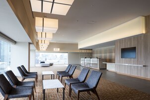 Egy modern szállodai előcsarnok, amelyben ülősarok, recepció és egy nagy ablak található, ahonnan a városra nyílik kilátás.
