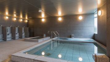 A modern indoor swimming pool with a stone floor and walls, surrounded by multiple shower cubicles.