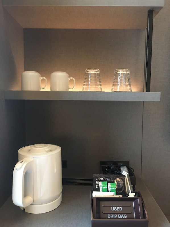 Una estación de café con una cafetera de goteo, una bolsa para café de filtro y una repisa con tazas y vasos.