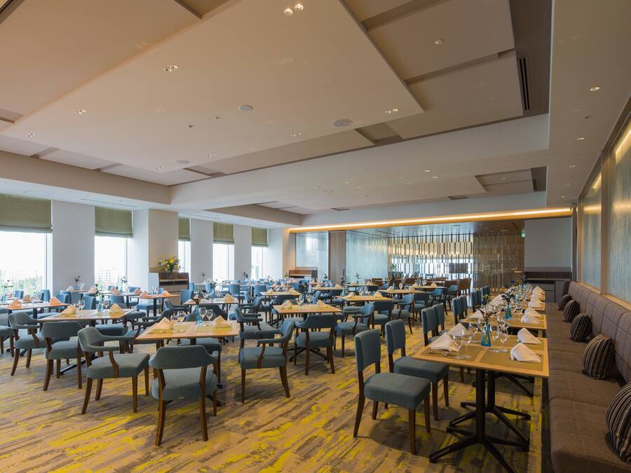 A spacious dining area with multiple tables and chairs, large windows, and a modern ceiling design.