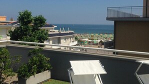 En takterrass med vita loungestolar, en liten trädgårdsdel och utsikt över stranden och havet.