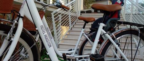Una bicicleta blanca con la marca 'HOTEL HOUSTON' estacionada cerca de una escalera.