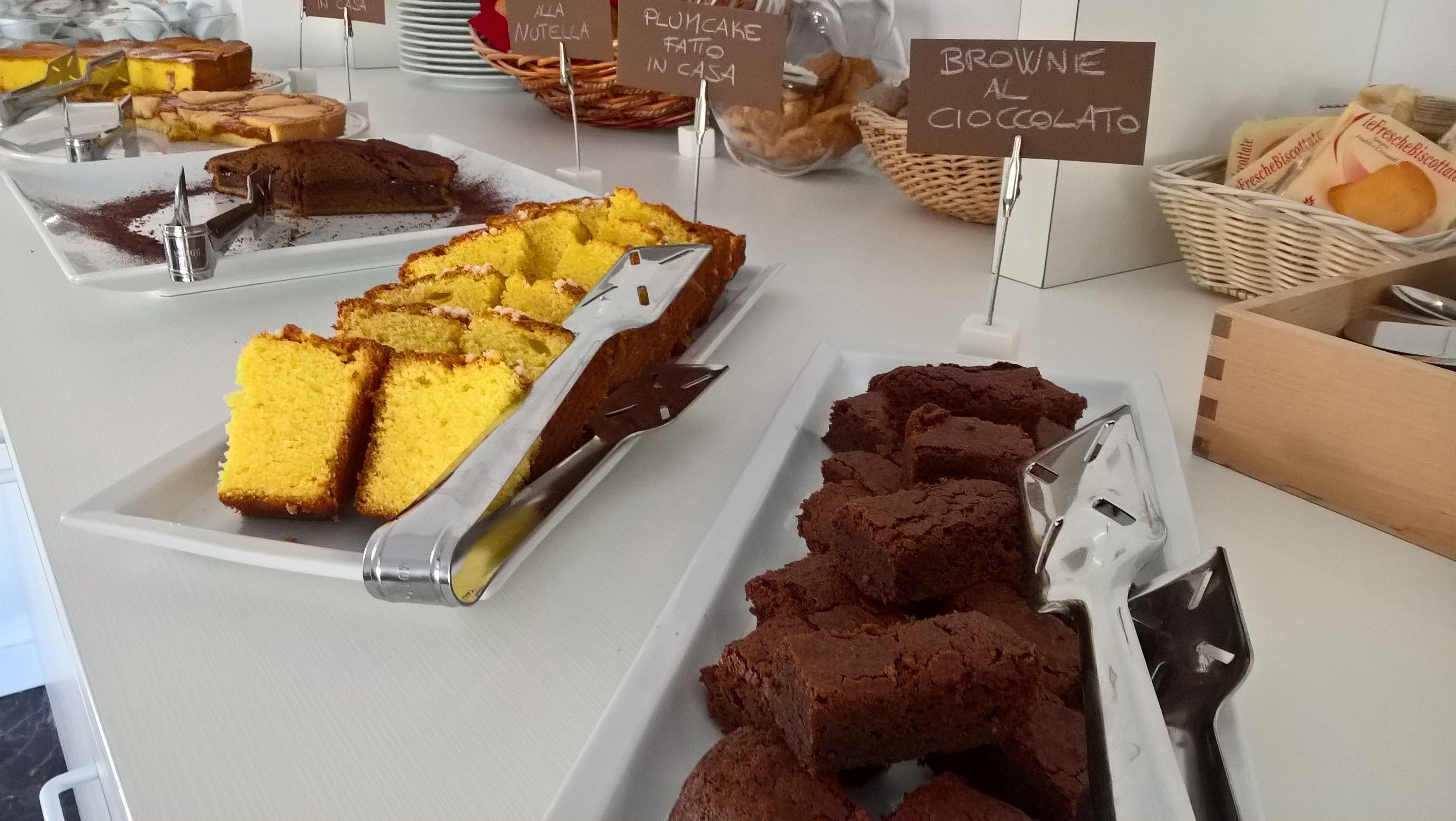 Een dessertvitrine met diverse taarten en gebak, waaronder gele chiffoncake en brownies, voorzien van handgeschreven bordjes.