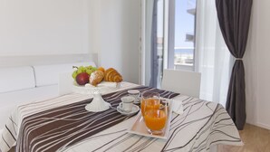En frukostuppsättning med croissanter, frukt och apelsinjuice på ett bricka, ett vitt bord och utsikt över naturen genom ett fönster.