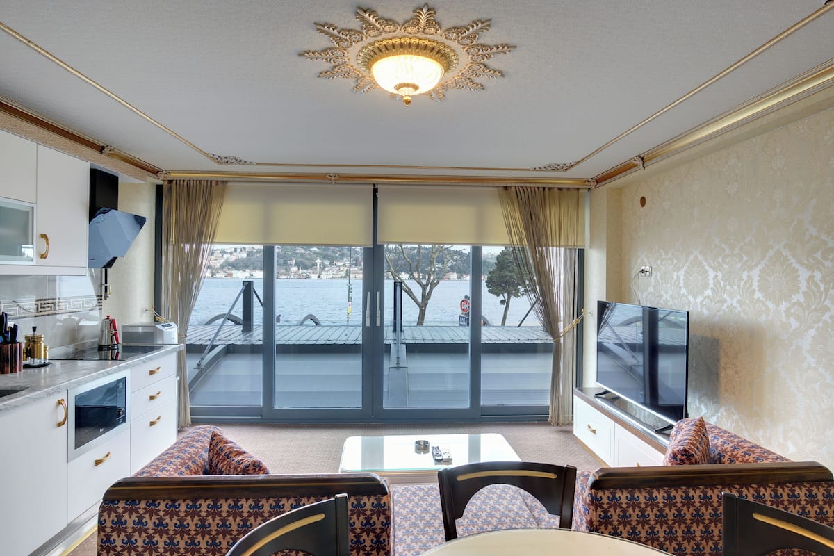 A hotel room with a balcony, a television, a dining area, and a kitchen.