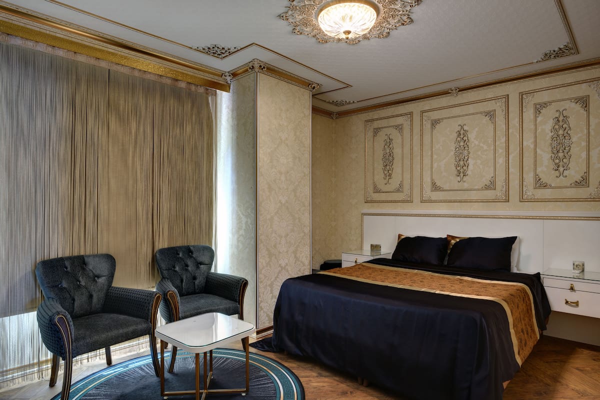 A hotel room with a large bed, two armchairs, a small table, and a large window with curtains.
