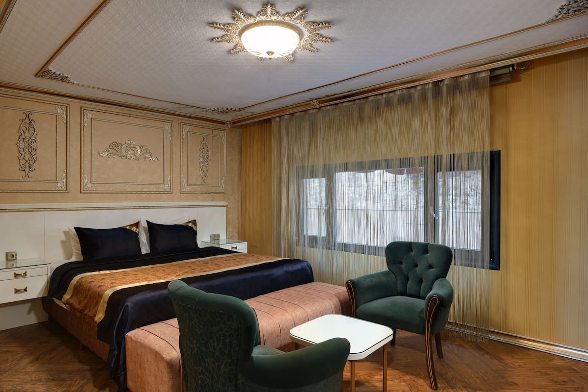A hotel room with a large bed, two chairs, a small table, and a large window with curtains.