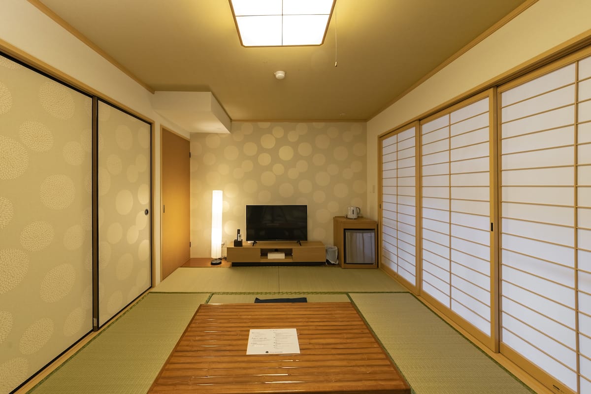 Um quarto japonês tradicional com tatames, uma televisão, um armário e portas deslizantes.