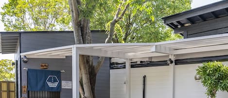 Un patio techado con una mesa y sillas de madera, un árbol y un edificio con puerta de garaje.