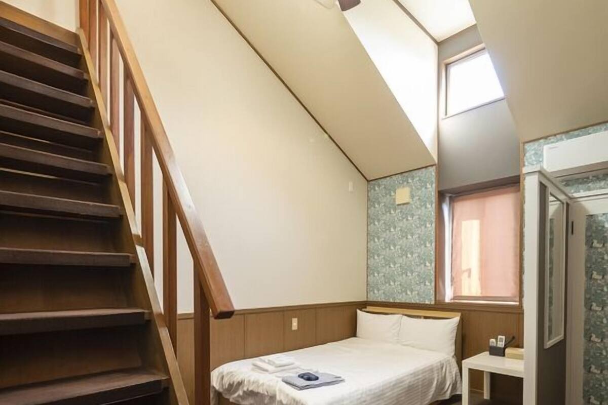 Quarto com cama, mesa de cabeceira, escada de madeira e ventilador de teto.