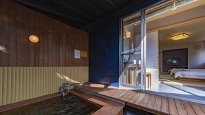 Een houten wellnessruimte met een whirlpool, een houten terras en een glazen deur naar een slaapkamer met een bed en een televisie.