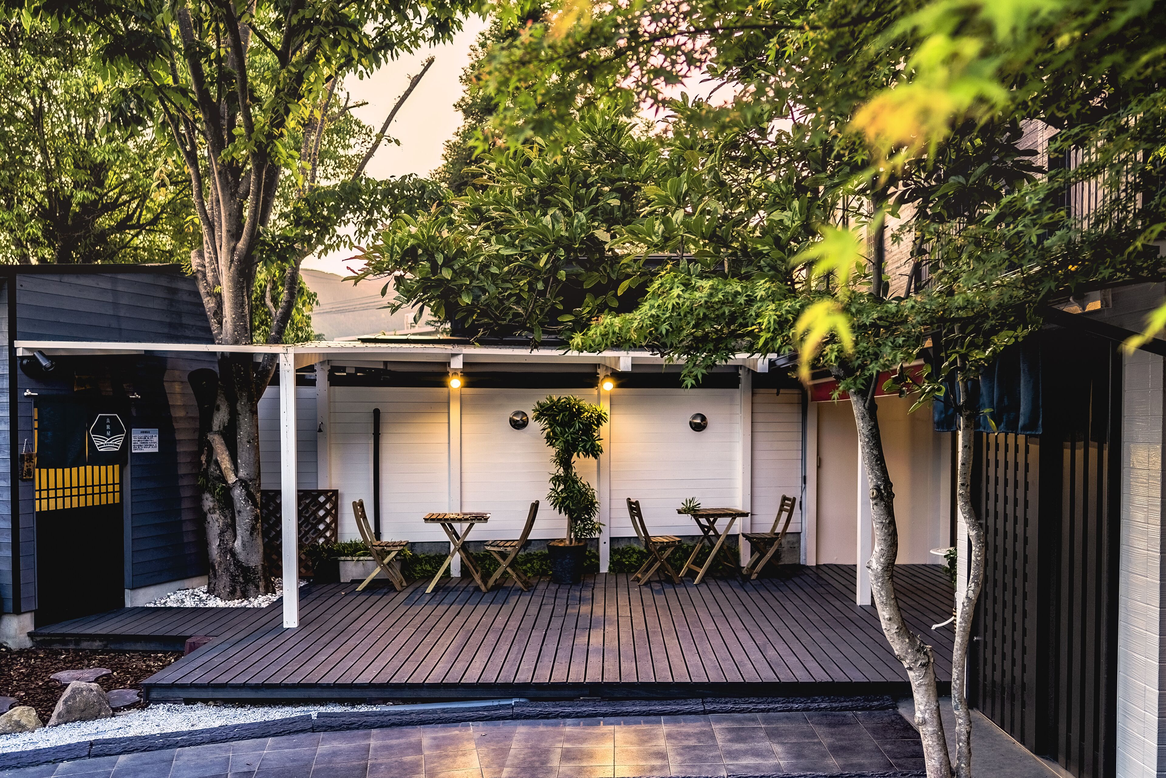 A covered patio area with wooden flooring, a seating arrangement, and a potted plant.