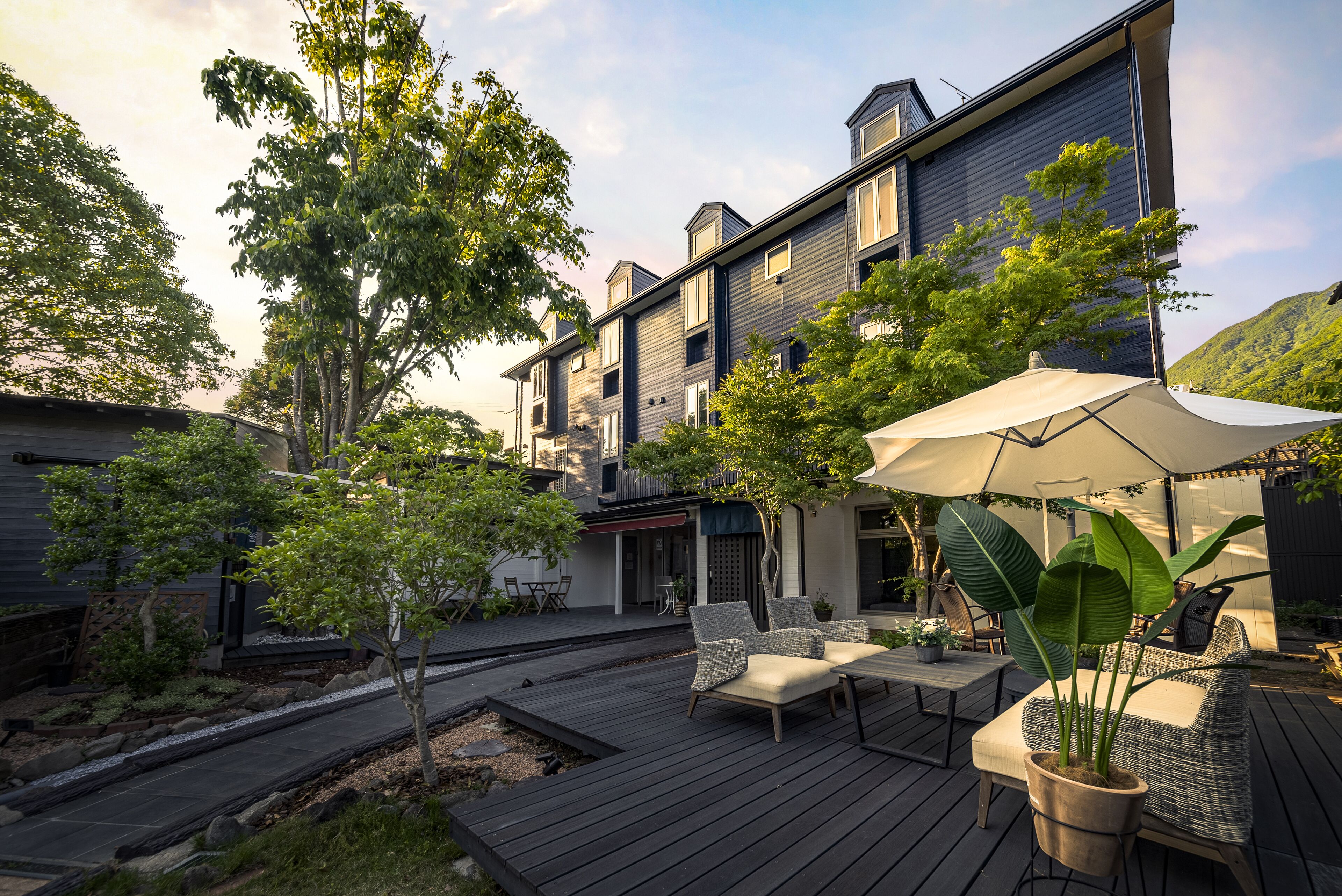 Un patio exterior moderno con cubierta de madera, mobiliario para exteriores y plantas en macetas.
