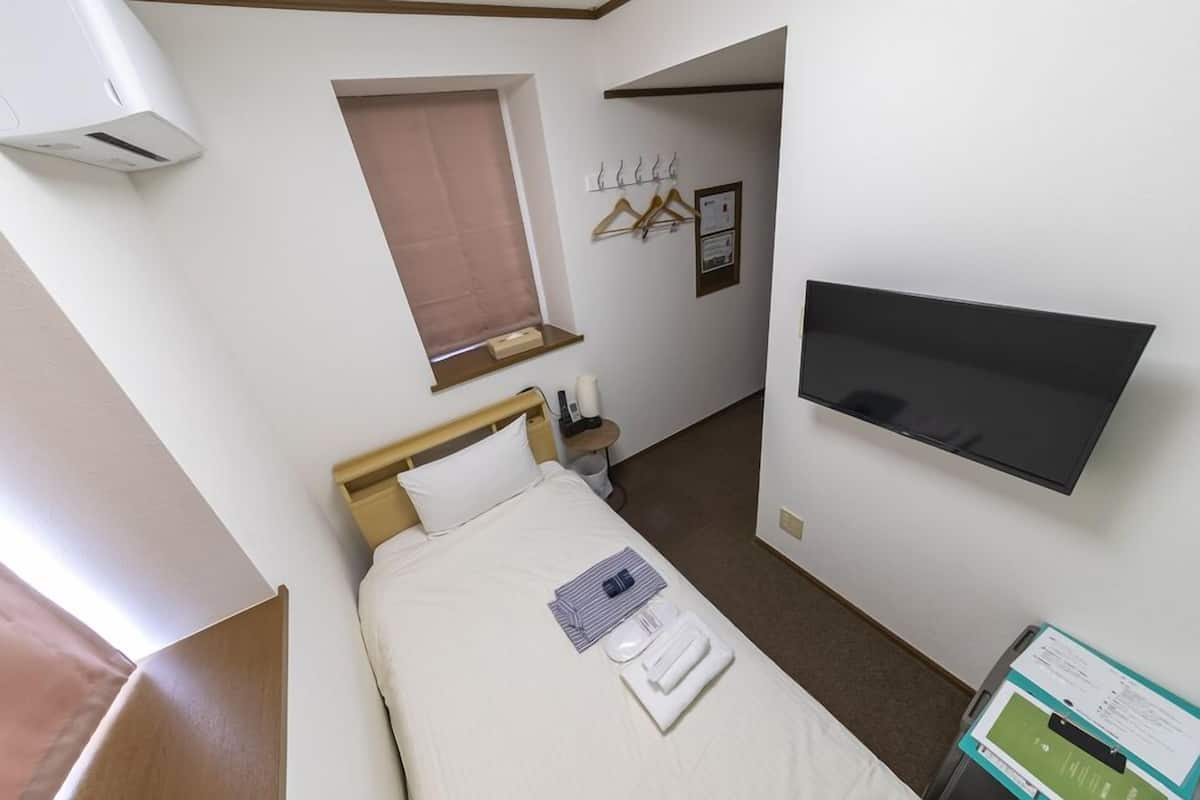 Quarto de hotel com cama, televisão na parede, janela com cortina e cabides num porta-roupas.