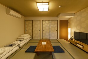 Ett traditionellt japanskt rum med tatamimattor på golvet, ett lågt träbord, futonmadrasser, skjutdörrar och en tv.